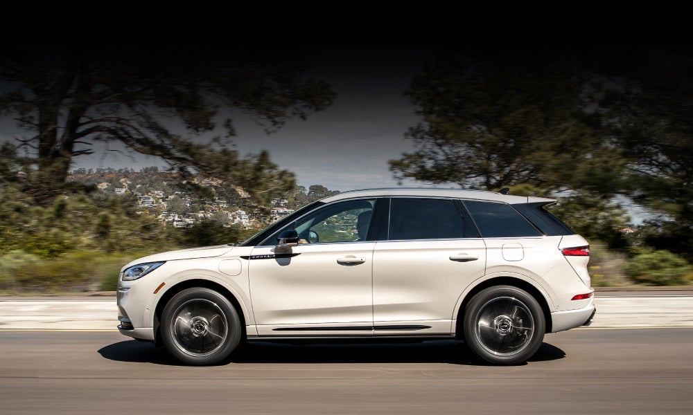 A 2021 Lincoln Corsair Grand Touring in Pristine White is being driven on a freeway as blue skies and sunlit trees grace the edges of the road