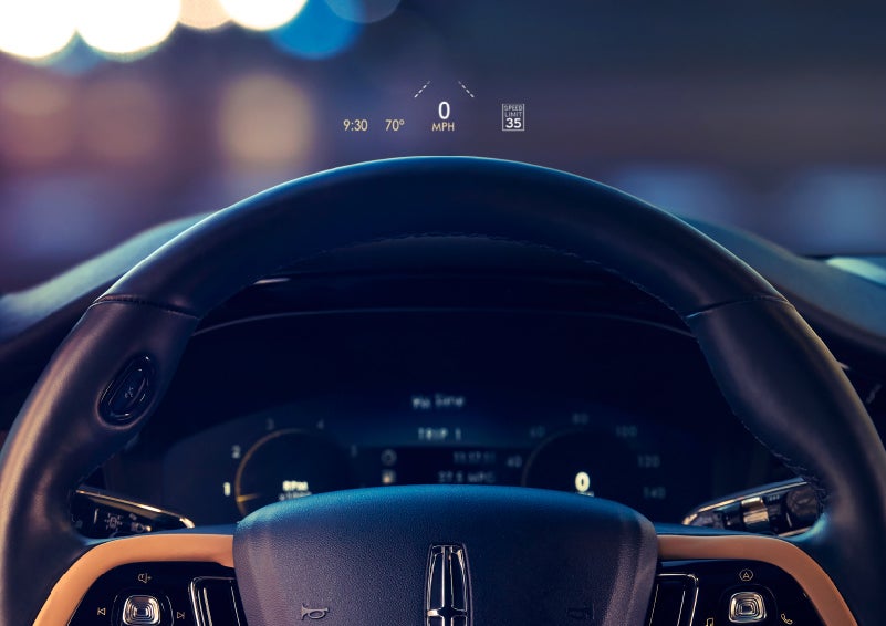 The available head-up display projects data on the windshield above the steering wheel inside a 2022 Lincoln Corsair as the driver navigates the city at night | Bedford Lincoln PA in Bedford PA