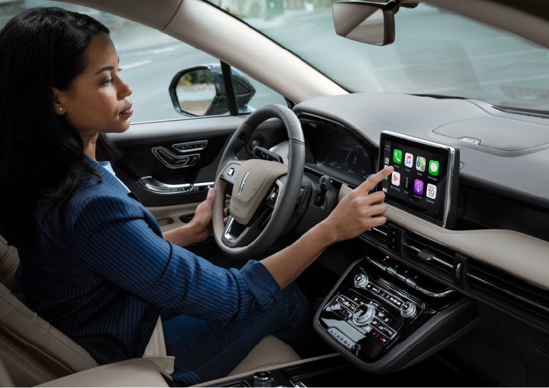 A woman in the driver's seat of a 2022 Lincoln Corsair is touching the center digital screen to connect to Apple CarPlay® | Bedford Lincoln PA in Bedford PA