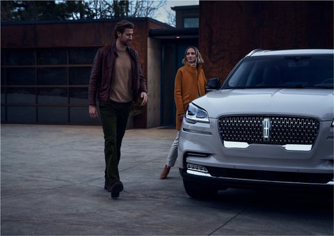 A man and a woman approaching a 2023 Lincoln Aviator® SUV, which illuminates certain lights when they are close | Bedford Lincoln PA in Bedford PA