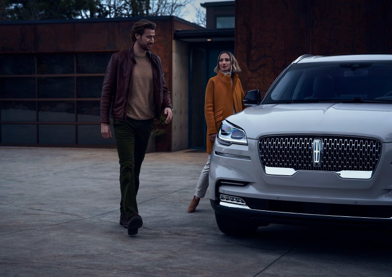 A man and a woman approaching a 2024 Lincoln Aviator® SUV, which illuminates certain lights when they are close | Bedford Lincoln PA in Bedford PA