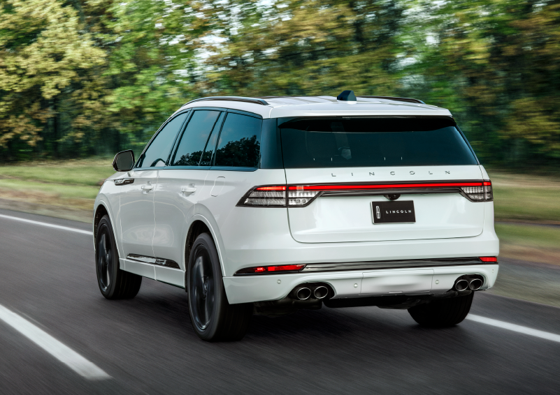 A white 2025 Lincoln Aviator® SUV is being driven away down a road lined with colorful trees. | Bedford Lincoln PA in Bedford PA