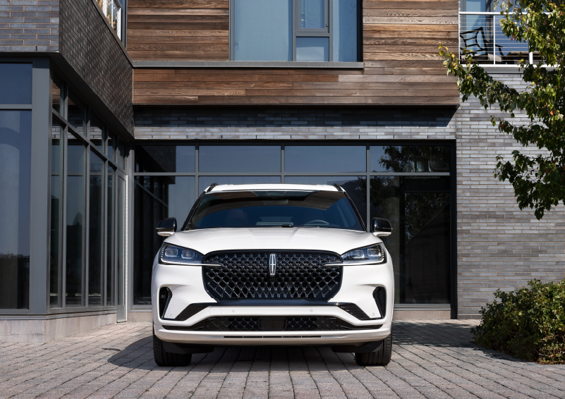 A white 2025 Lincoln Aviator® SUV is shown parked outside a modern building with gray brick and wood accents. | Bedford Lincoln PA in Bedford PA
