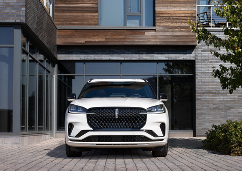 A white 2025 Lincoln Aviator® SUV is shown parked outside a modern building with gray brick and wood accents. | Bedford Lincoln PA in Bedford PA