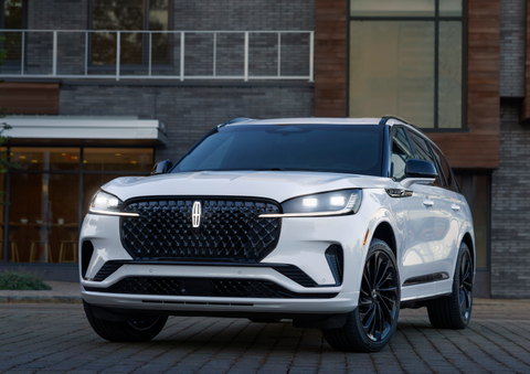 A white 2025 Lincoln Aviator® SUV is shown parked outside a modern building with gray brick and wood accents. | Bedford Lincoln PA in Bedford PA
