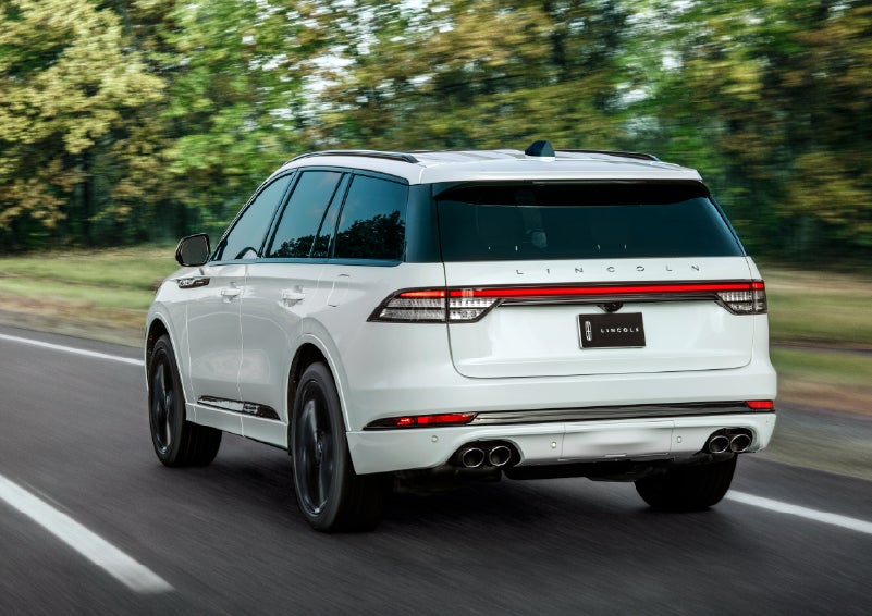 A white 2026 Lincoln Aviator® SUV is being driven away down a road lined with colorful trees. | Bedford Lincoln PA in Bedford PA
