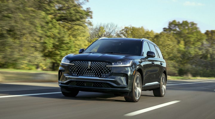 A 2026 Lincoln Black Label™ Aviator® SUV is being driven down a road lined with trees. | Bedford Lincoln PA in Bedford PA
