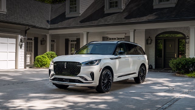 A white 2026 Lincoln Aviator® SUV is parked in the driveway of a luxury home. | Bedford Lincoln PA in Bedford PA