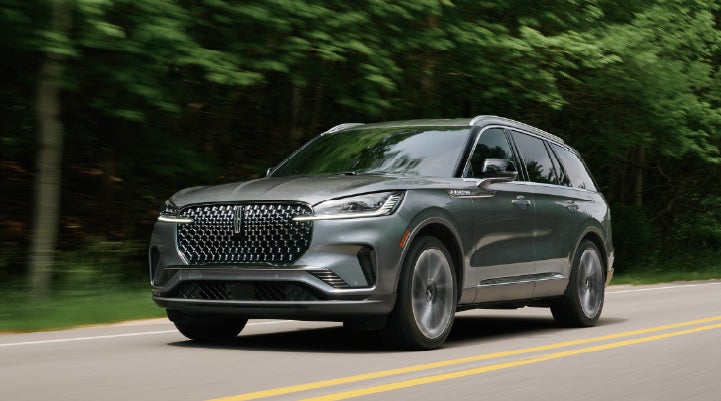 A 2027 Lincoln Aviator® SUV is being driven down a road lined with trees. | Bedford Lincoln PA in Bedford PA